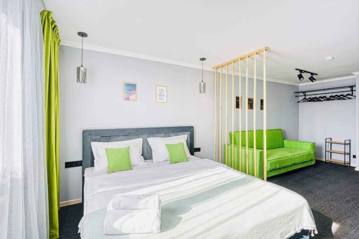 Una habitación de hotel moderna con cama, sofá verde y un separador de madera.