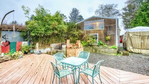Un terrazza in legno con tavolo e sedie, immersa nel verde e con un edificio decorato da un murale.