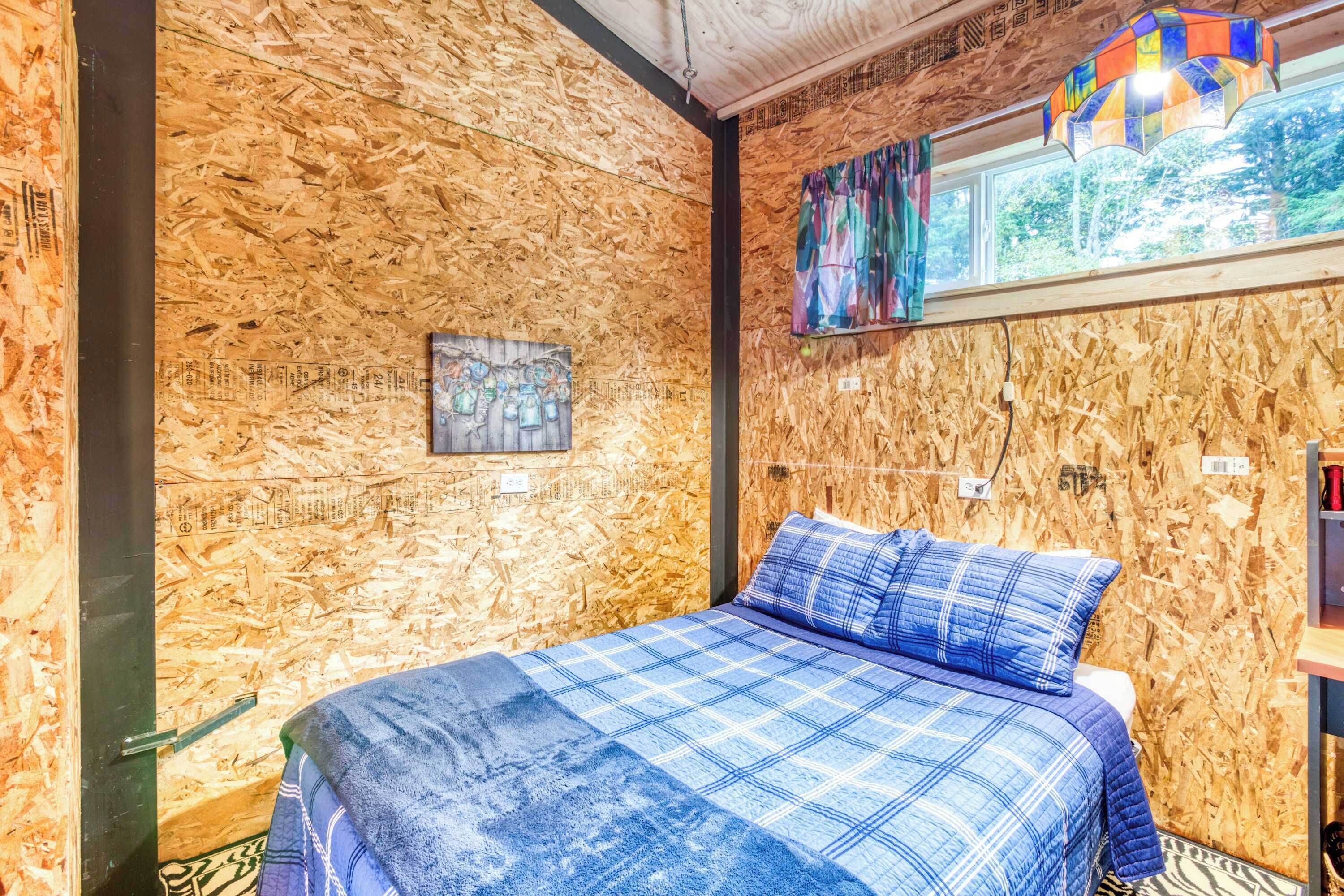 A room with a bed, wooden walls, a window with a view, and a colorful hanging light fixture.