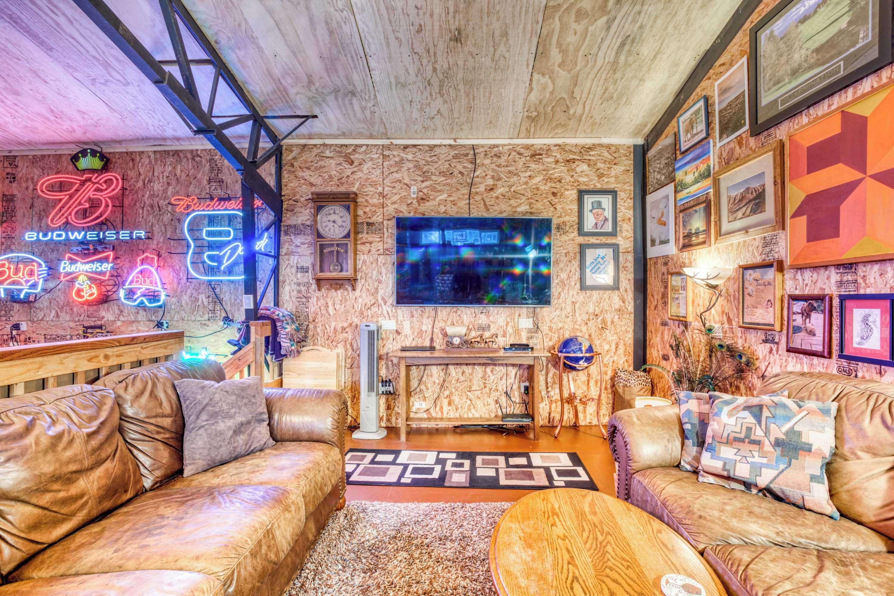 A cozy living room with a wooden ceiling, leather sofas, a coffee table, a TV, and neon Budweiser signs.