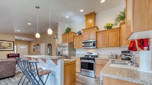 A modern kitchen with wooden cabinets, stainless steel appliances, and a bar area with stools.