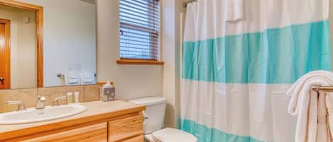 Un baño con tocador de madera, un lavamanos blanco, un inodoro y una cortina de ducha a rayas azul y blanco.