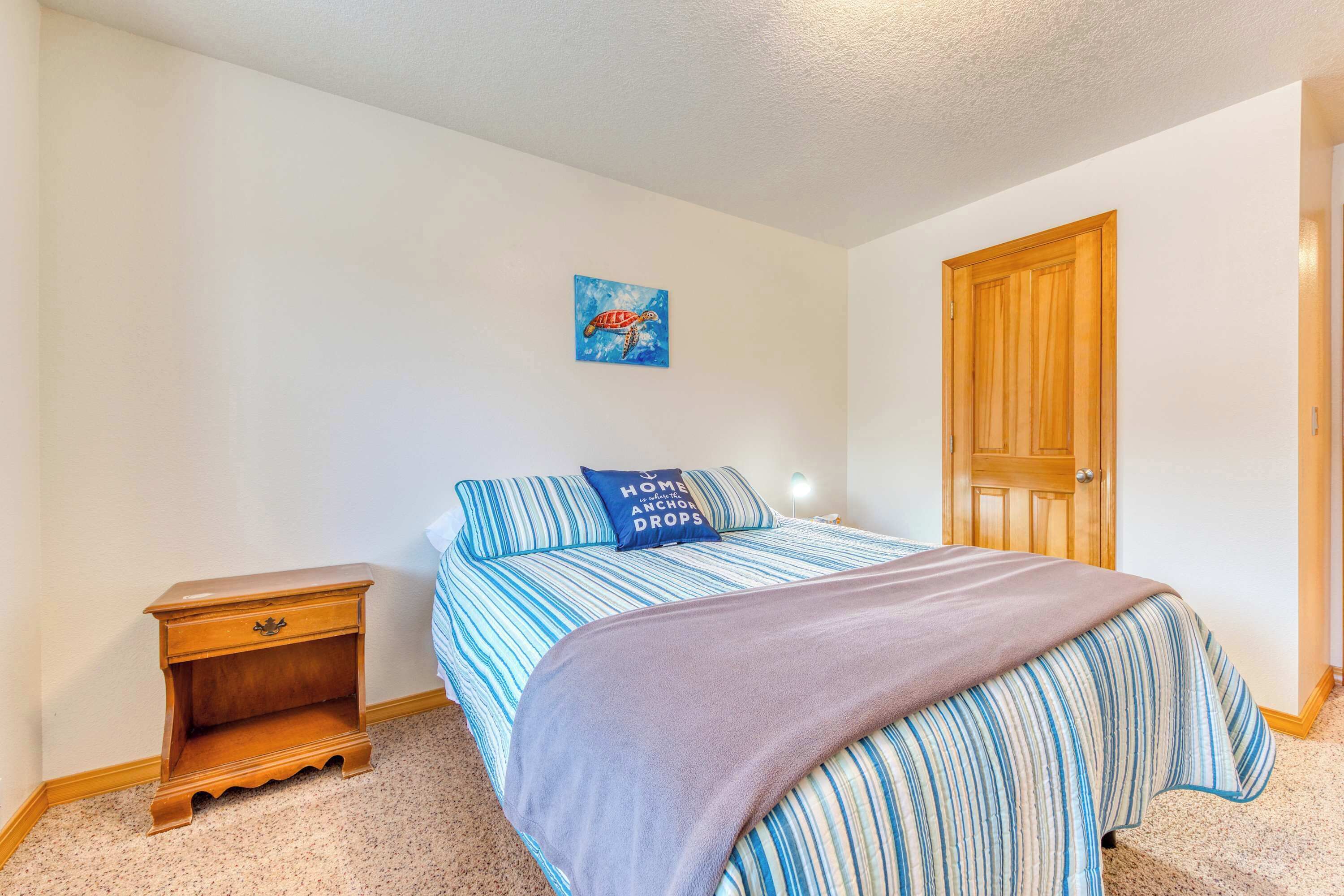 A bedroom with a bed, a nightstand, a door, and a wall with a painting.