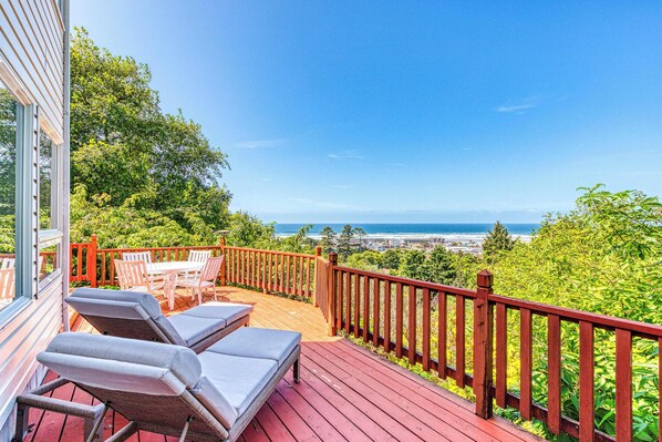 A wooden deck with lounge chairs and a table, overlooking a scenic view of the ocean and greenery. - Relax and Enjoy Expansive Ocean Views from Your Own Private Retreat (Rockaway Beach)