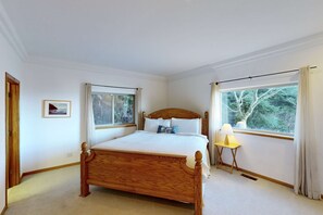A bedroom with a wooden bed, two windows, a bedside table with a lamp, and a framed picture on the wall. - Relax and Enjoy Expansive Ocean Views from Your Own Private Retreat (Rockaway Beach)