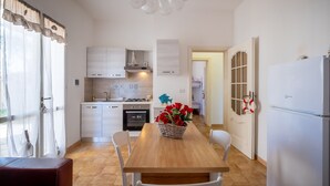 A compact kitchen with white cabinets, a dining table with chairs, and a refrigerator. - Holiday Home 'Villa Serèa' with Shared Garden and Air Conditioning (Scala di Furno)