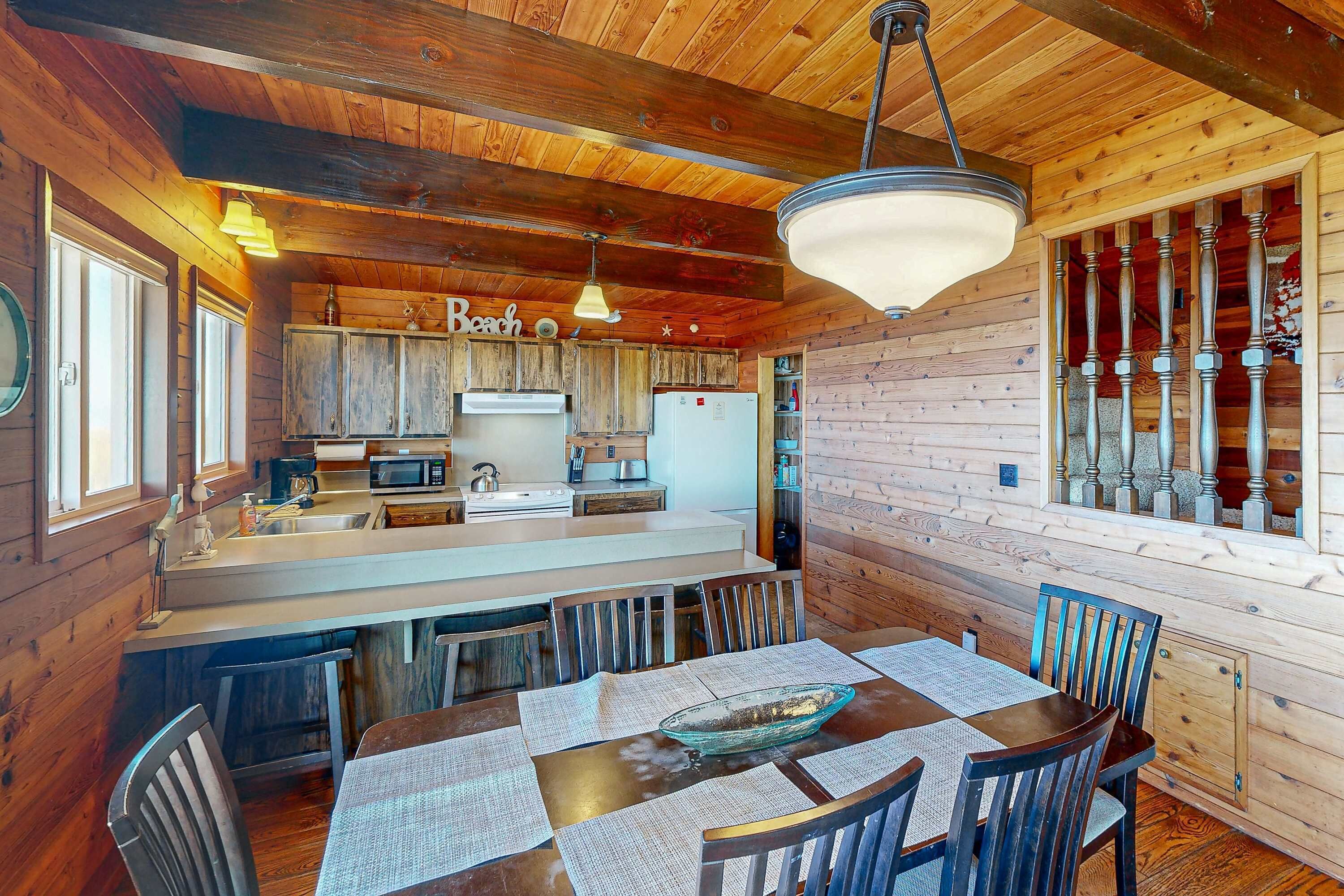 A wooden cabin with a kitchen featuring a large island, bar stools, and a dining table with placemats.