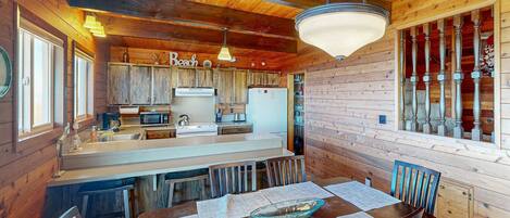 A wooden cabin with a kitchen featuring a large island, bar stools, and a dining table with placemats.
