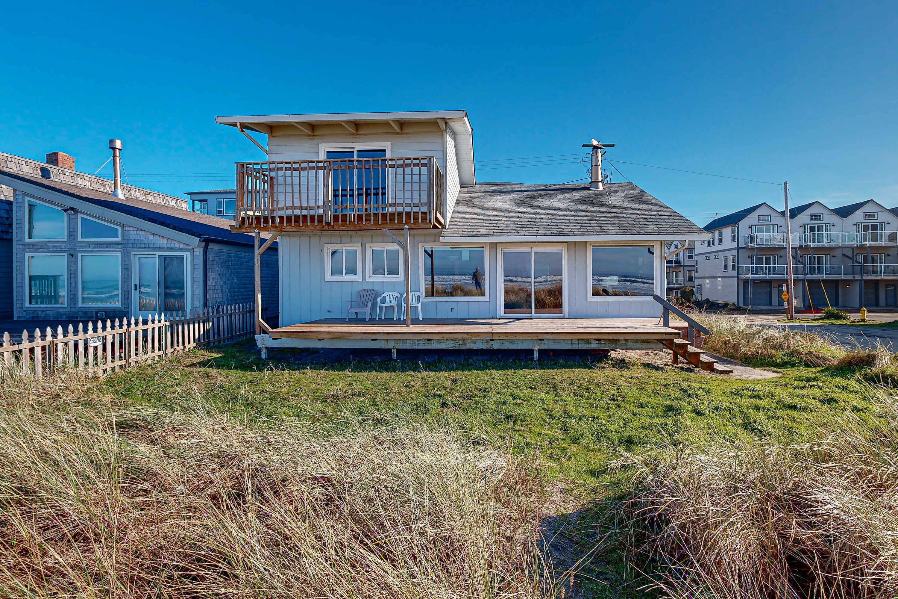 A coastal house with a balcony, a deck, and a view of the beach.