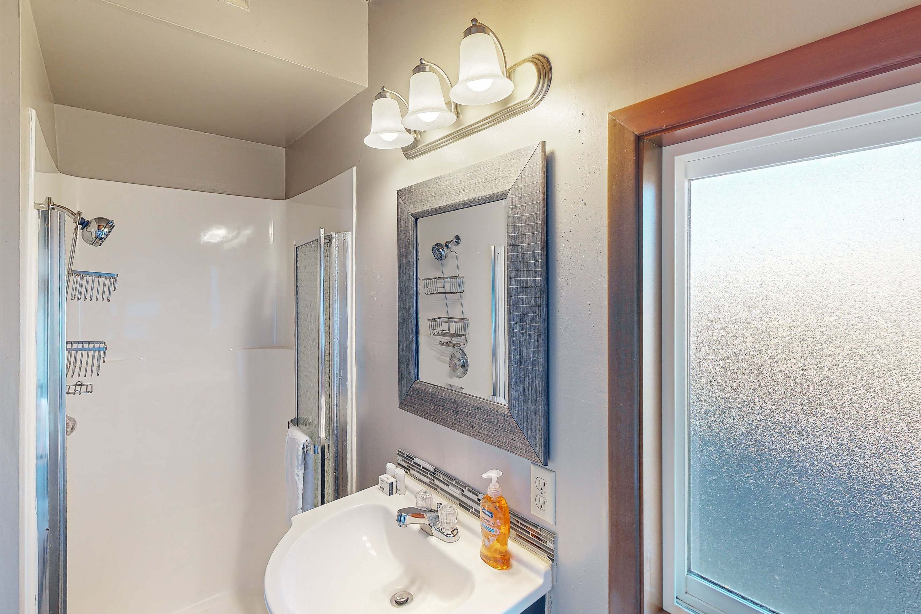 Een badkamer met een witte wastafel, een spiegel en een douche met een glazen deur.