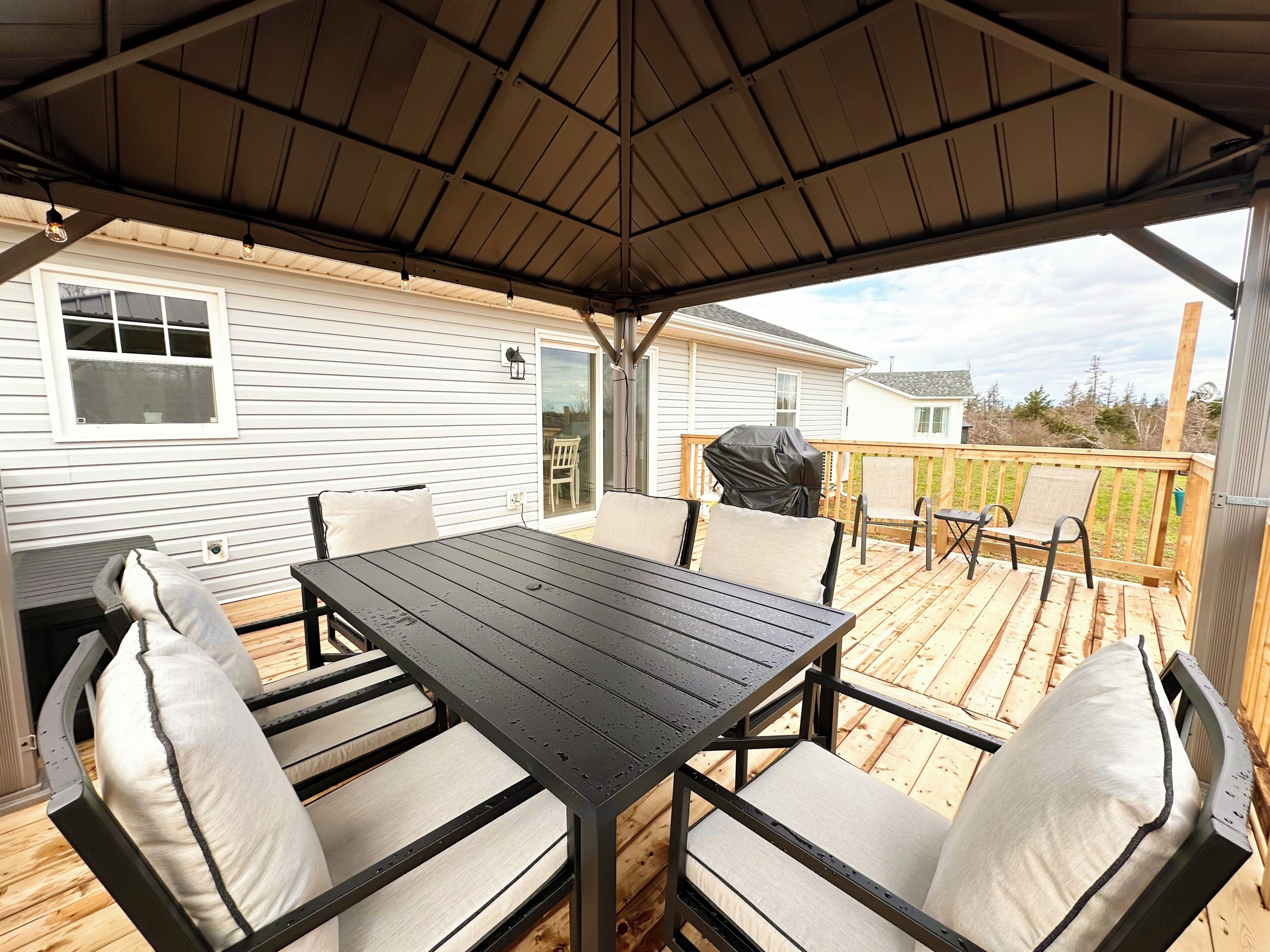 A covered patio with a table and chairs, a grill, and a view of a house.
