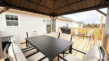 A covered patio with a table and chairs, a grill, and a view of a house.