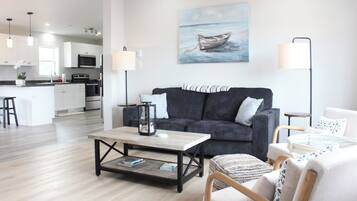 A modern living room with a grey sofa, a coffee table, and a painting of a boat on the wall.