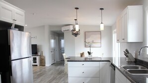 Una cocina moderna con armarios blancos, un refrigerador de acero inoxidable, una encimera negra e iluminación colgante.