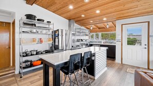 Une cuisine moderne dotée d’un îlot central, d’appareils électroménagers en acier inoxydable et d’un plafond en bois.
