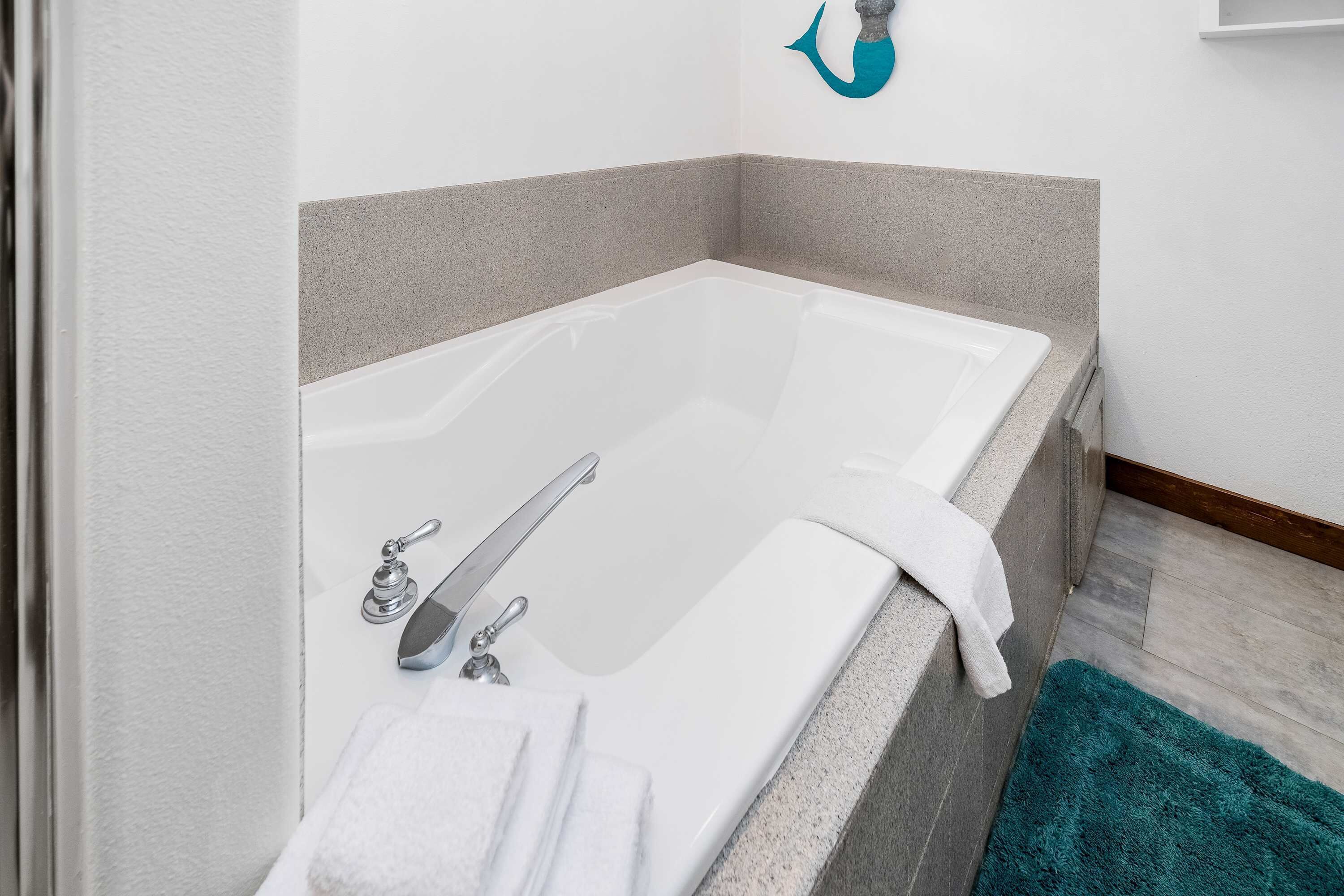A modern bathroom with a freestanding bathtub, a towel rack, and a teal bath mat.