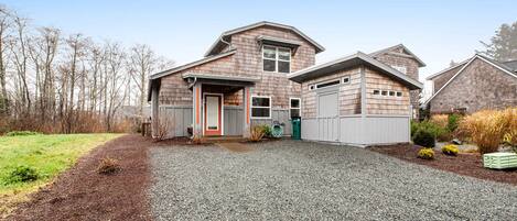 A two-story house with a gravel driveway and a front yard with mulch and plants.