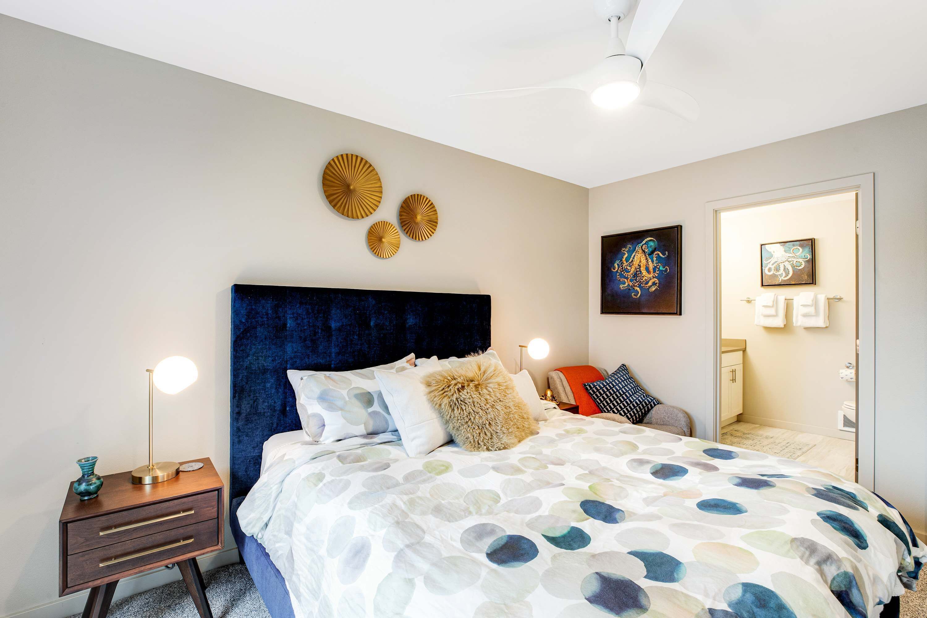 A bedroom with a large bed, a nightstand with a lamp, and a ceiling fan.