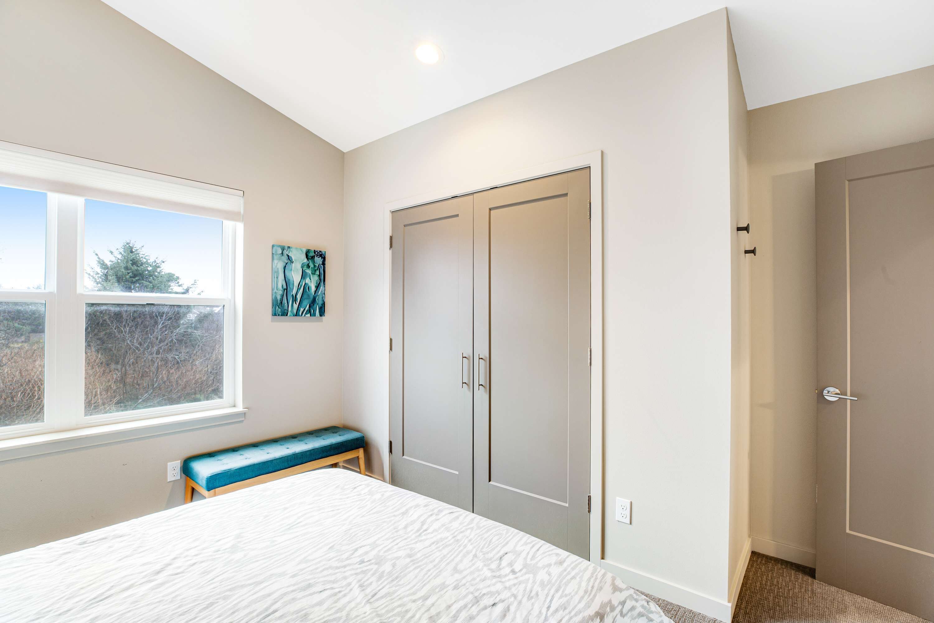 A bedroom with a bed, a bench, a wardrobe, and a window with a view of trees.