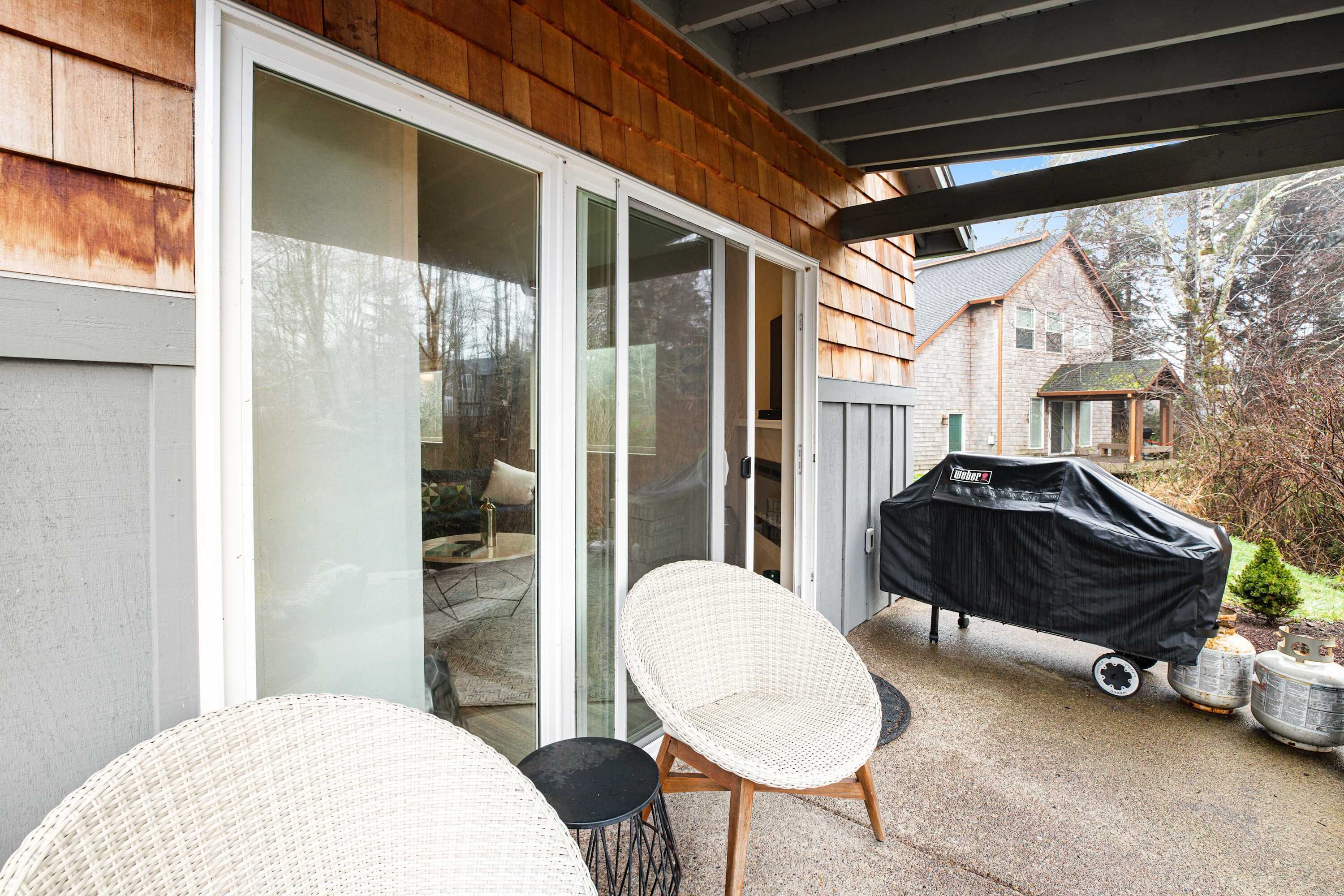 A covered patio with wicker chairs, a barbecue grill, and sliding glass doors leading to a patio area.