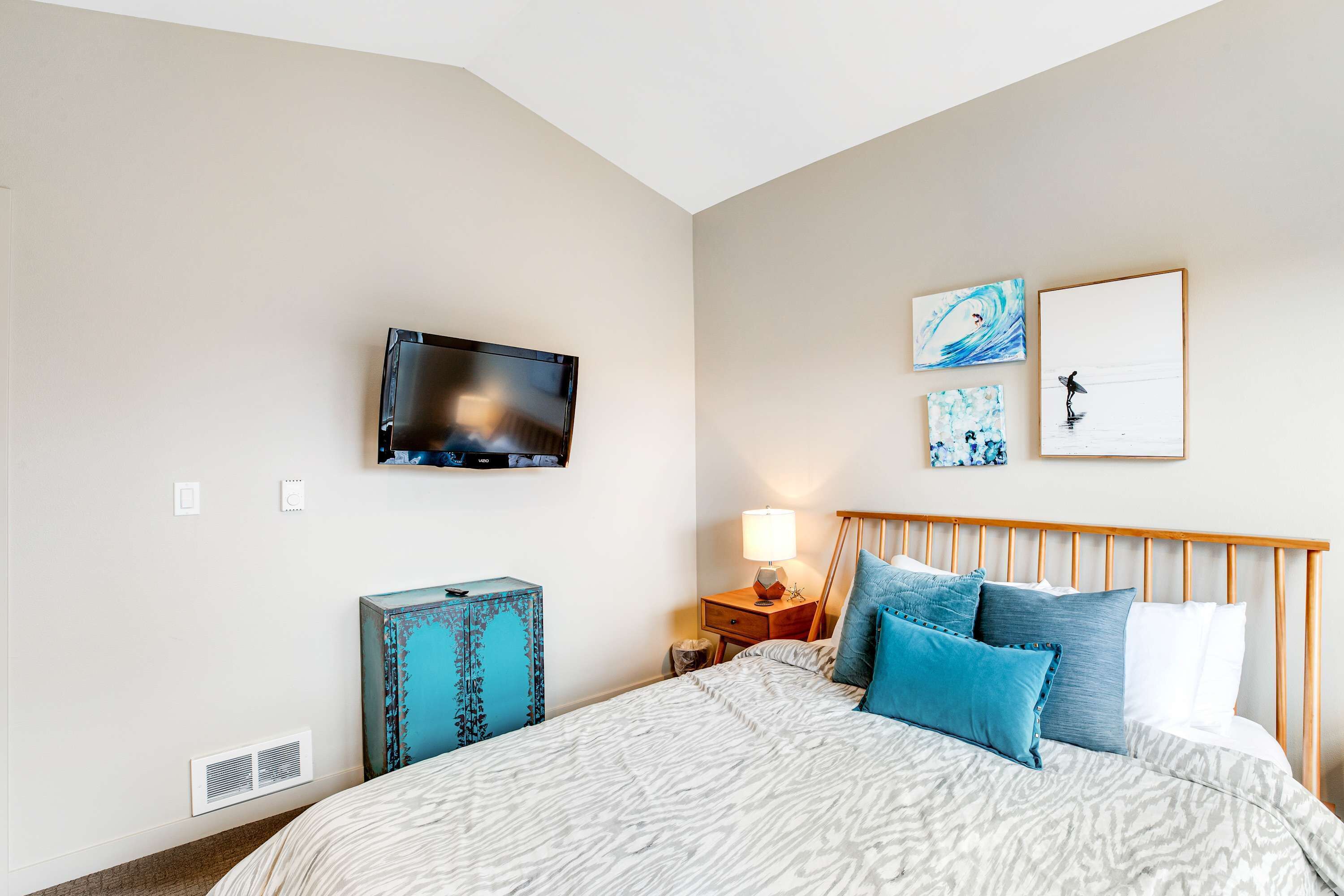Un dormitorio con cama, televisor montado en la pared y obras de arte.
