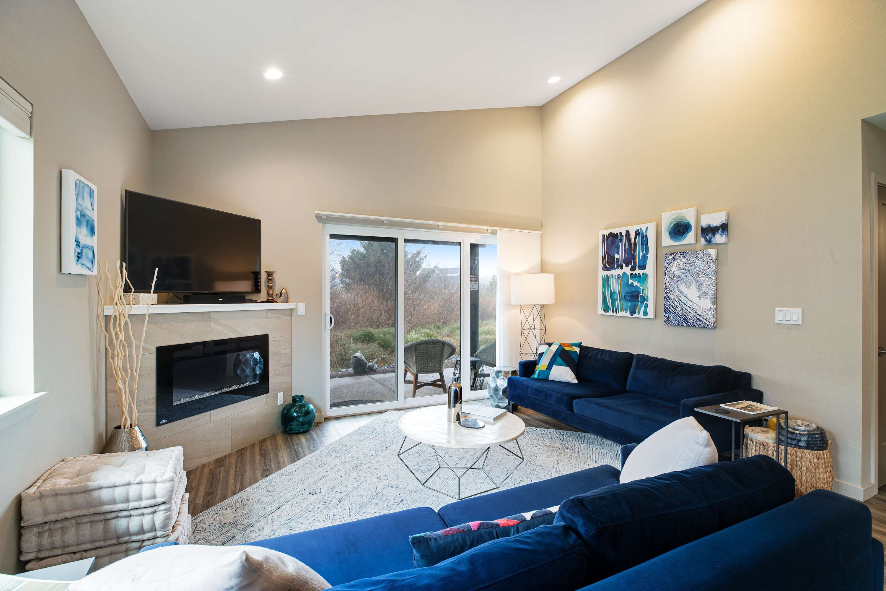A modern living room with a fireplace, a large TV, a blue sofa, and a dining area with a table and chairs.
