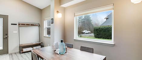 Ein Essbereich mit einem Holztisch, Stühlen und einer Bank. Ein Fenster bietet Blick auf ein Haus und Bäume.