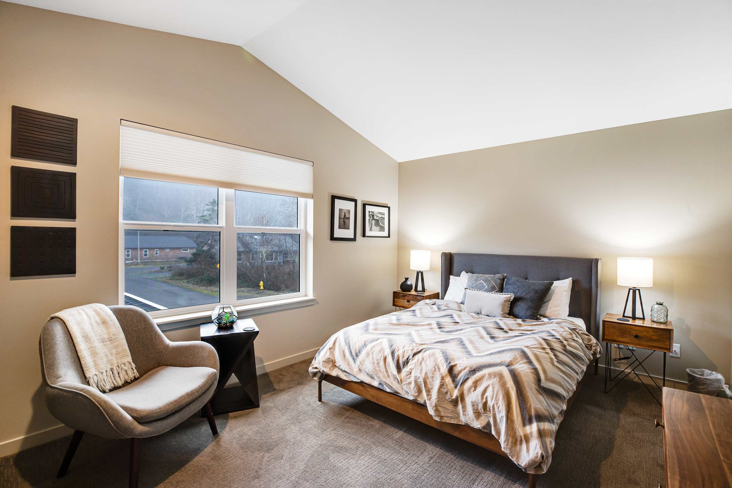 A bedroom with a bed, a chair, a nightstand, and a window.