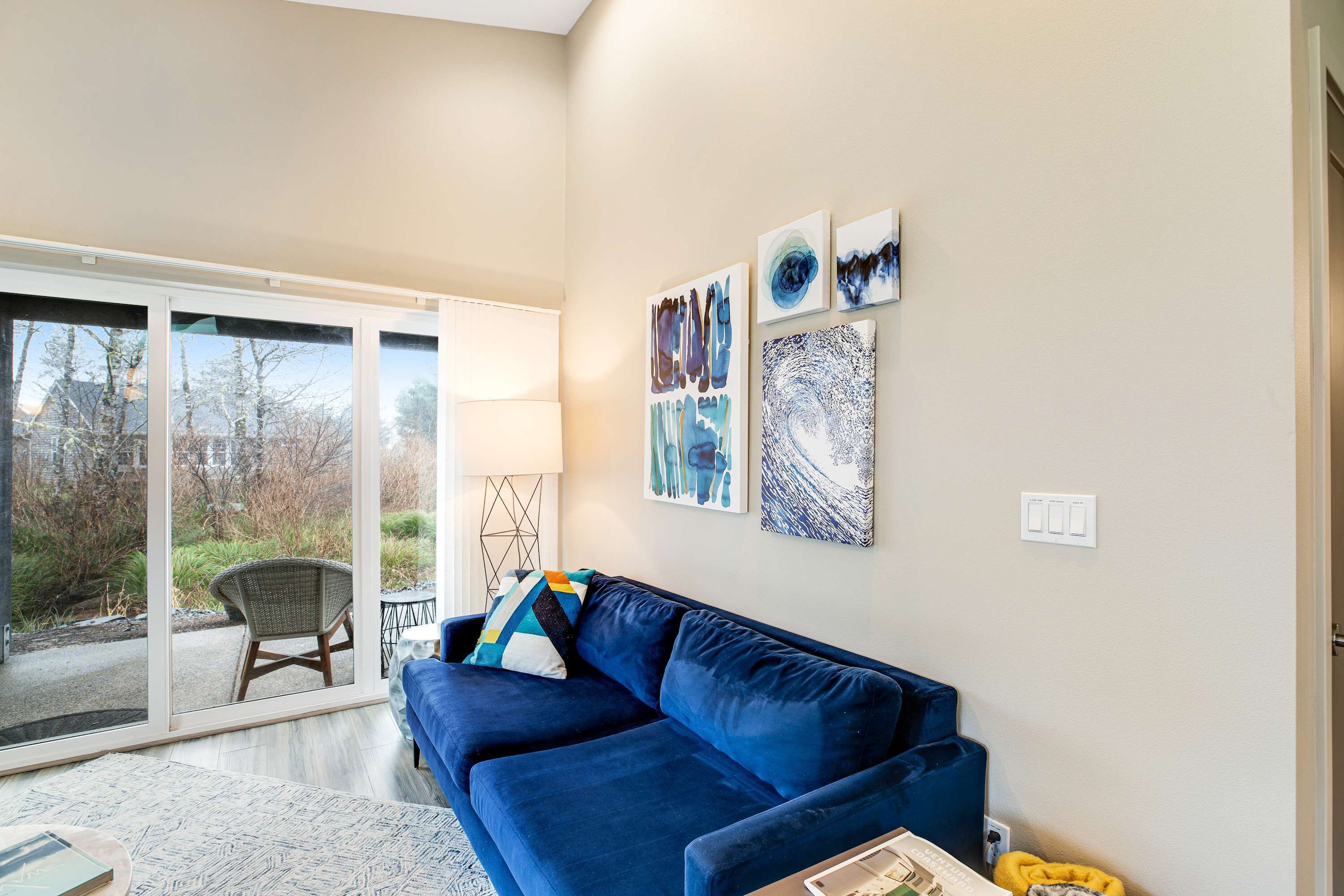 Un soggiorno moderno con un divano blu, una porta vetrata che dà su un patio e opere d'arte astratte alle pareti.
