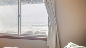 Una habitación con cama, ventana con cortinas y vista al mar.