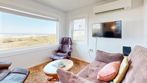 A living room with a large window, a leather chair, a sofa, and a flat-screen TV. - Quaint Beach Getaway with Beach Access Ocean View and Perfect Location Near Town (Rockaway Beach)