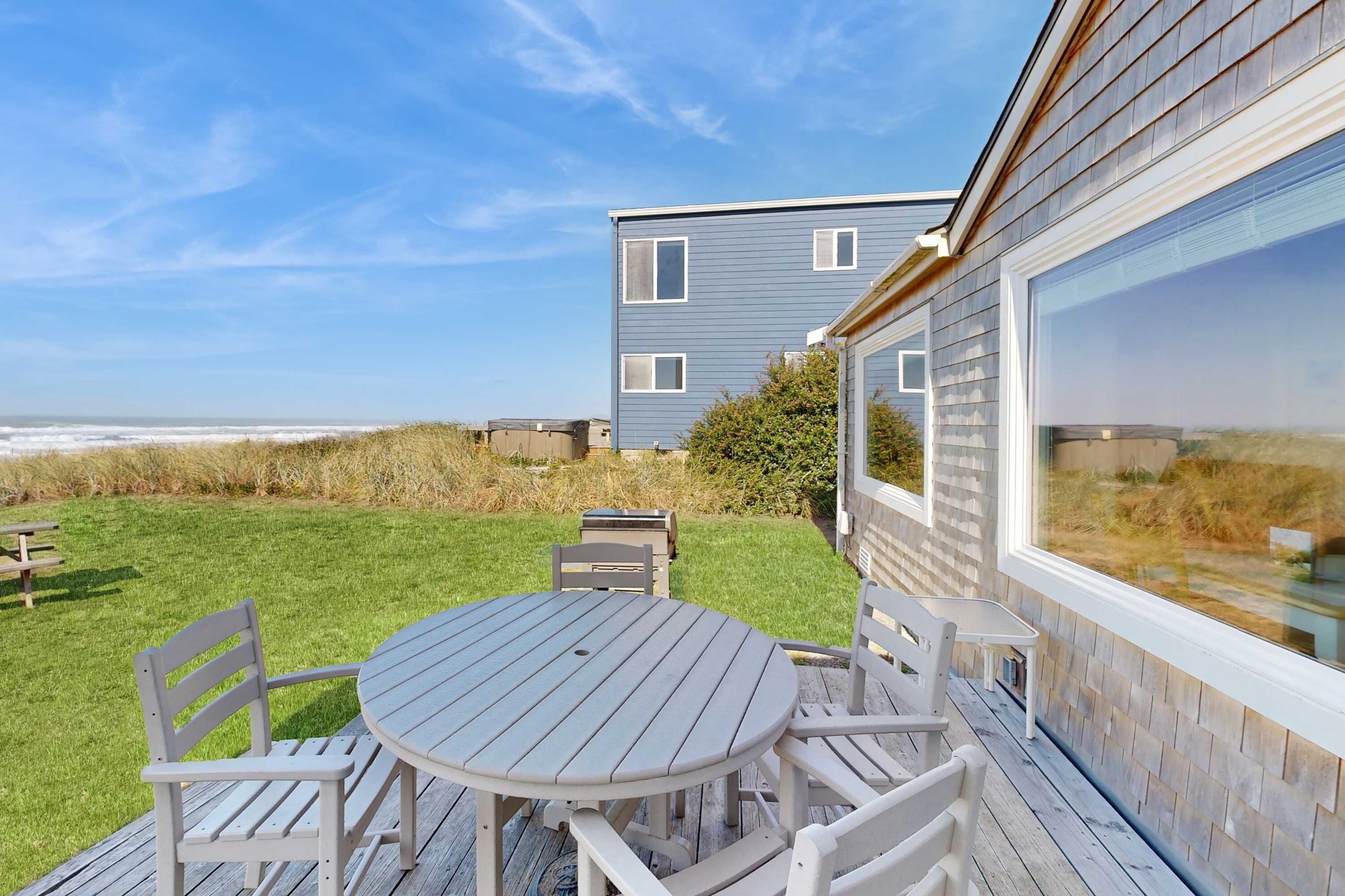 A deck with a table and chairs, overlooking a beach and a building with large windows.