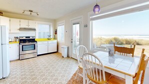 A kitchen with a stove, oven, and white cabinets. There is a dining table with chairs and a view of the beach. - Quaint Beach Getaway with Beach Access Ocean View and Perfect Location Near Town (Rockaway Beach)