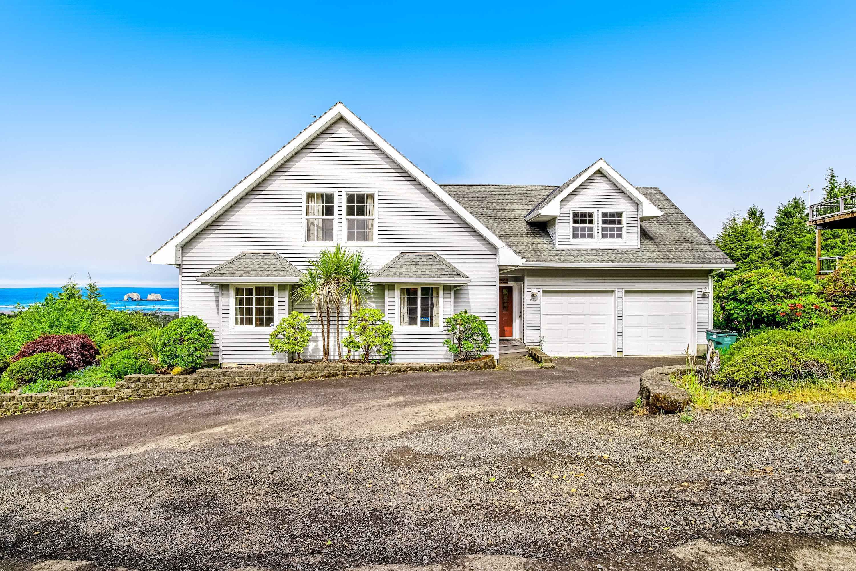 Een twee verdiepingen tellend huis met een garage, oprit en uitzicht op zee.