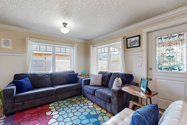 A cozy living room with a sectional sofa, a small wooden table, and a colorful rug. - Dog friendly beach home with firepit private hot tub beach access and arcade (Rockaway Beach)