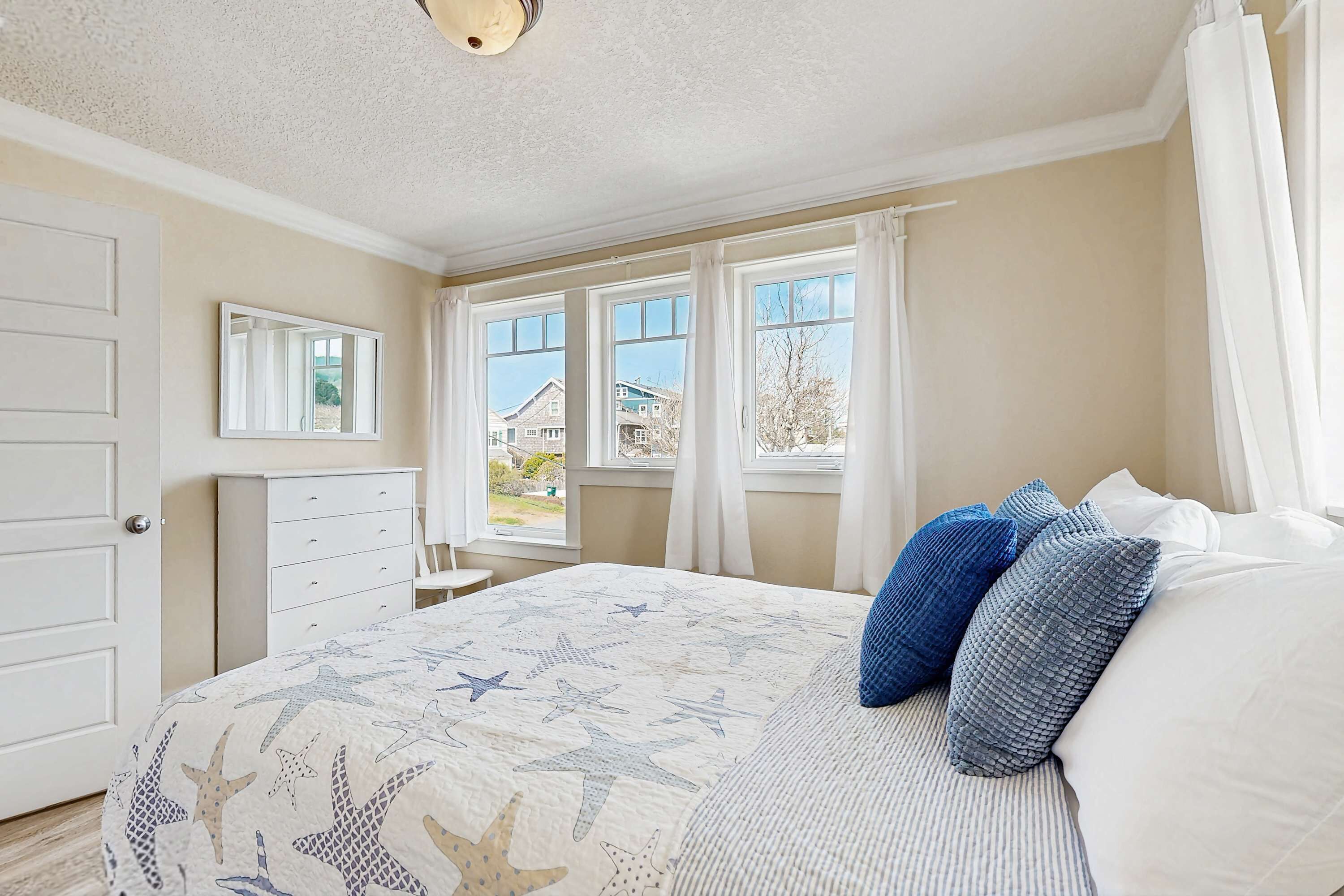 Un dormitorio con cama, cómoda, espejo y ventana con cortinas.