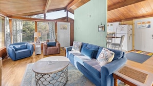 A cozy room with a blue sofa, a wooden ceiling, and a dining area with a table and chairs.