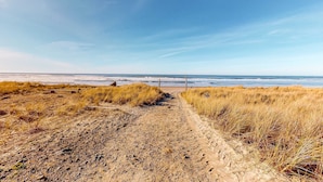 A sandy beach path leading to the ocean with dry grass on either side.