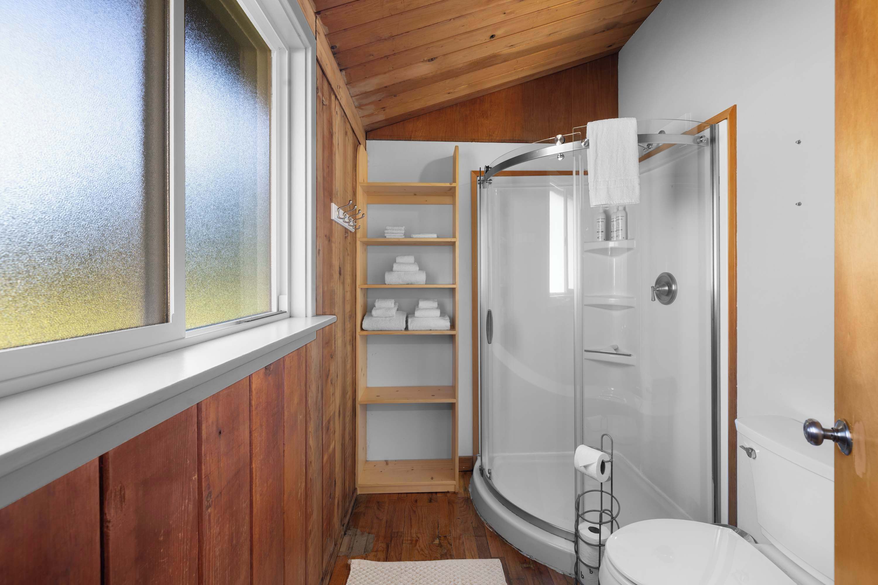 Une petite salle de bain dotée d’une douche à parois de verre, d’étagères en bois et de toilettes.