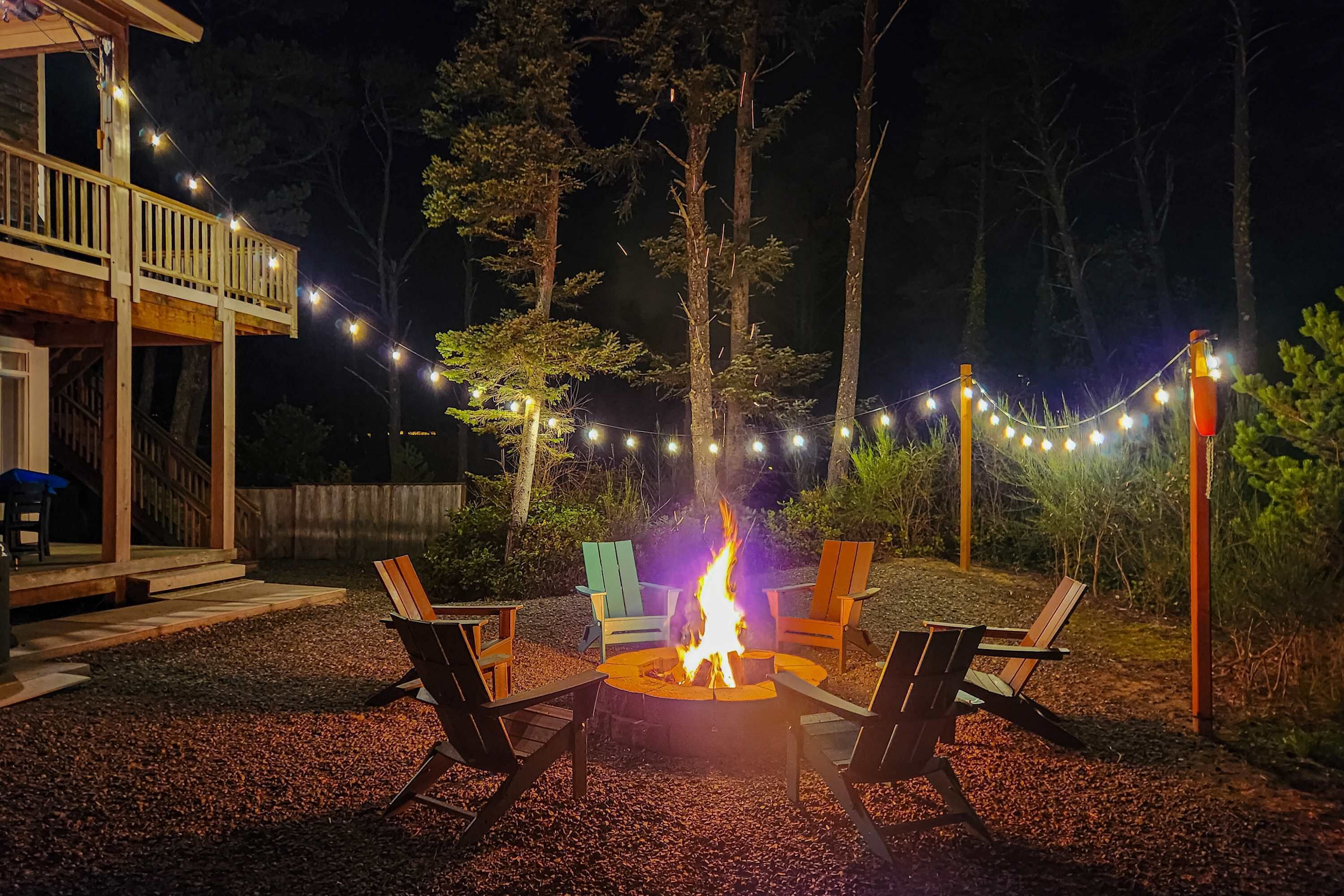 An outdoor seating area with a fire pit surrounded by chairs, string lights, and a deck.