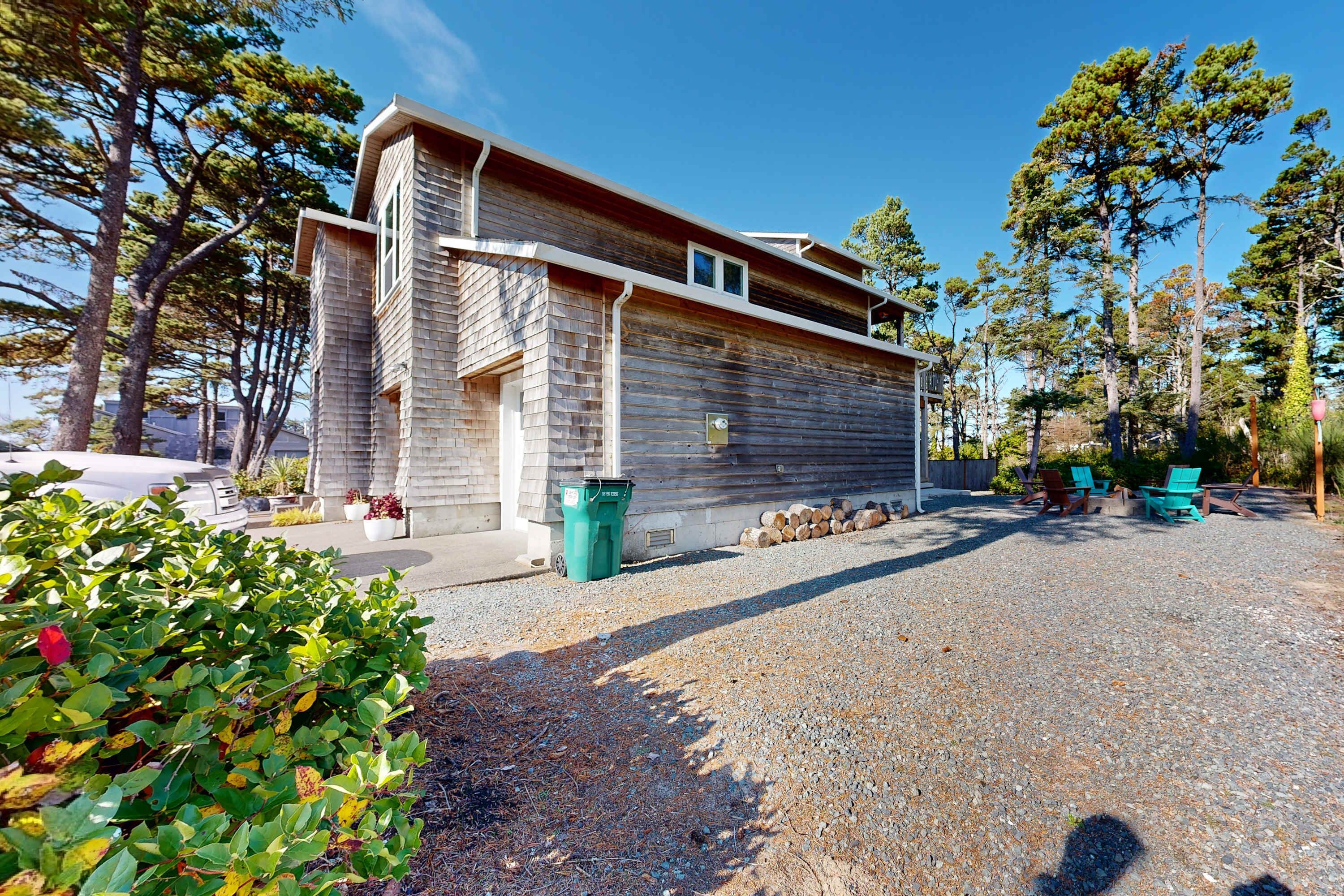 A wooden cabin with a gravel driveway, surrounded by trees and outdoor seating.