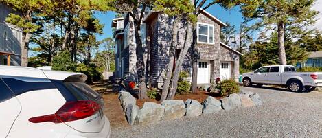 A residential area with houses, a white car, and a pickup truck parked on a gravel driveway.