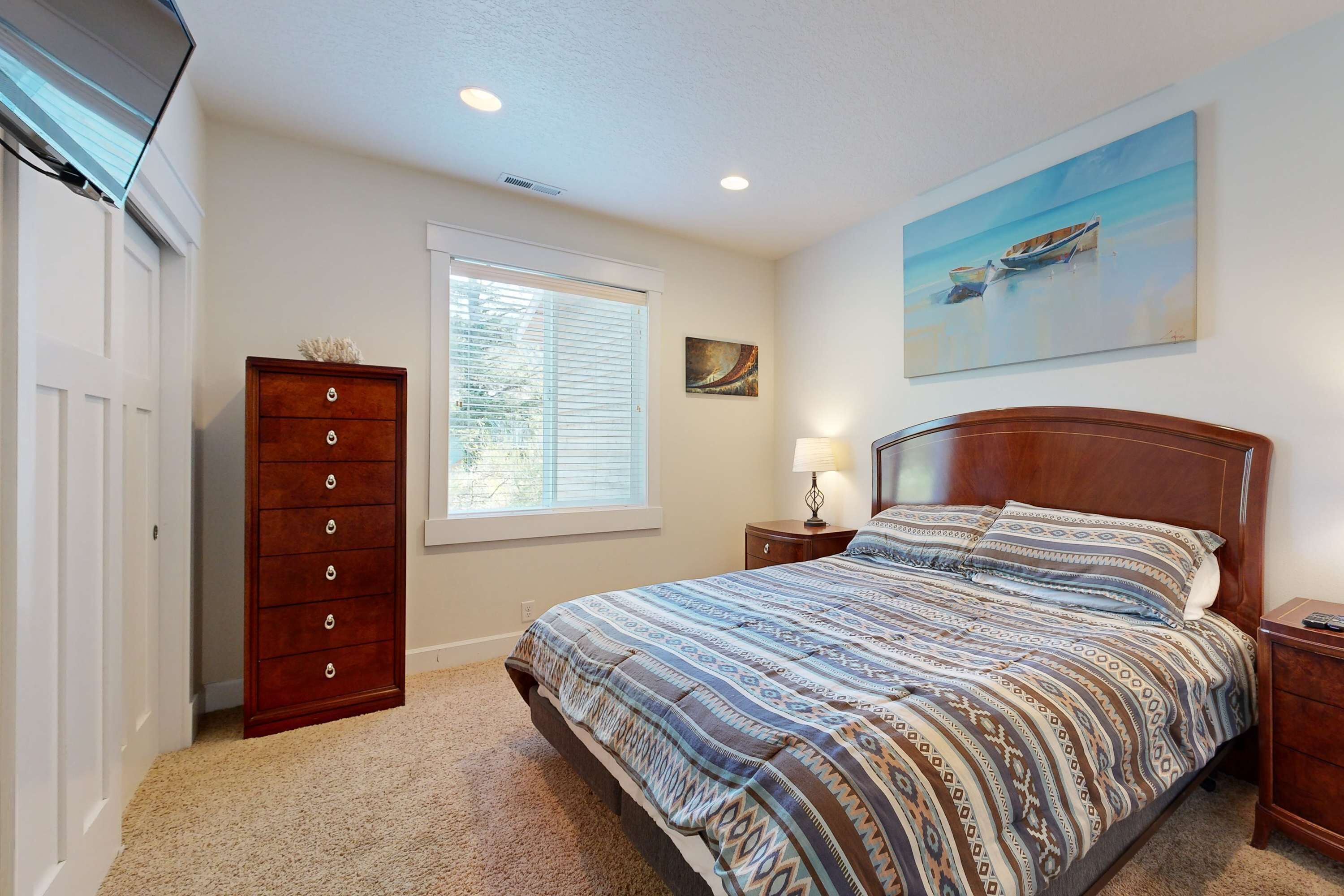 A bedroom with a bed, a dresser, a window, and a painting on the wall.