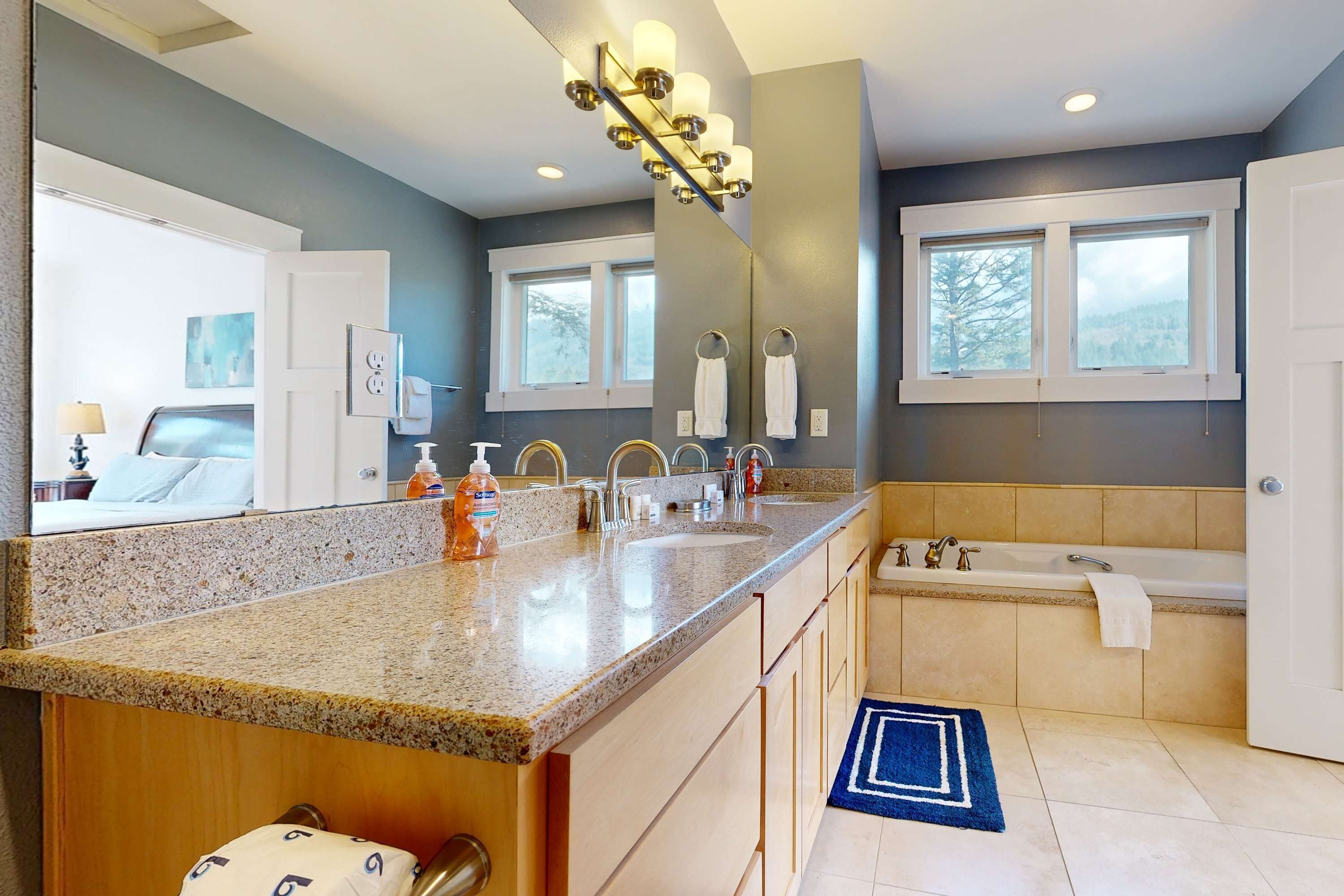 A modern bathroom with a granite countertop, dual sinks, a bathtub, and a large mirror.