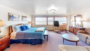 A bedroom with a bed, bedside table, lamp, dresser, and a view of the ocean. - Oceanfront Home with Great Ocean View Deck Fireplace Beach Access 2 Dogs OK (Rockaway Beach)