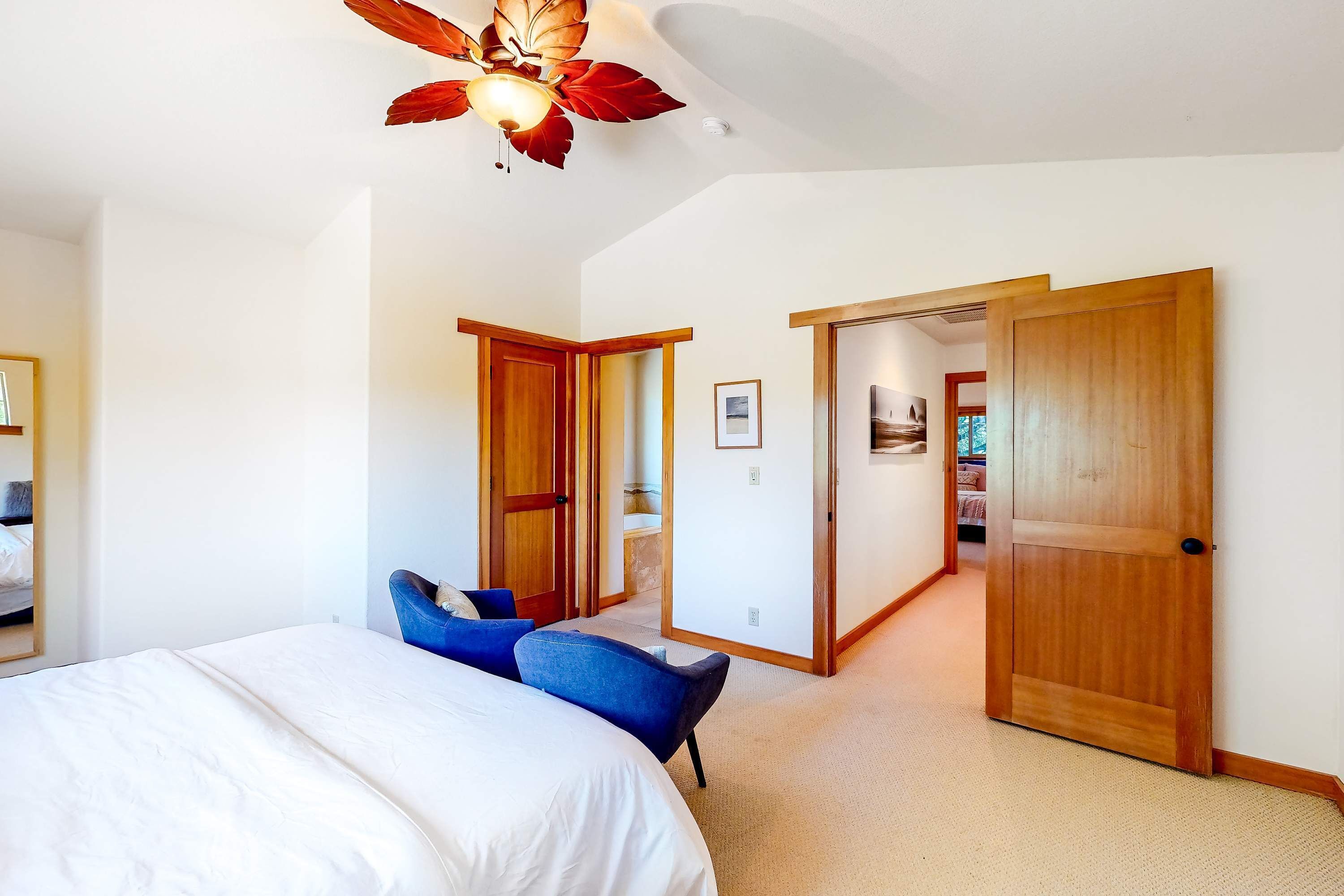 A bedroom with a large bed, two blue chairs, a ceiling fan, and wooden doors.