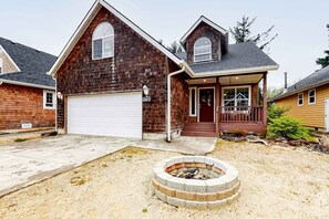 Une maison à deux étages avec un garage, une véranda et un foyer extérieur dans le jardin.