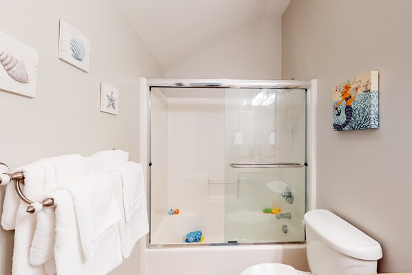 Un baño con ducha envuelta en vidrio, toallas blancas, un inodoro y decoración en la pared.
