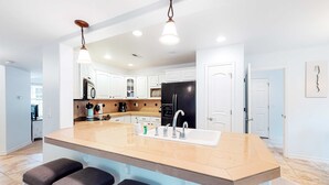 Una cocina moderna con una isla grande, taburetes de bar, un lavamanos y electrodomésticos de acero inoxidable.