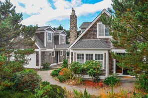 A two-story house with a stone chimney, a covered porch, and a well-maintained garden.